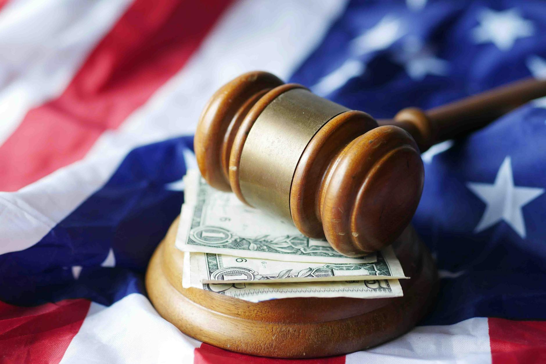 A gavel resting on dollar bills atop the American flag symbolizing justice and finance