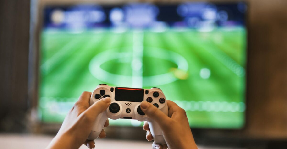 Close-up of hands holding a game controller playing a football video game on screen