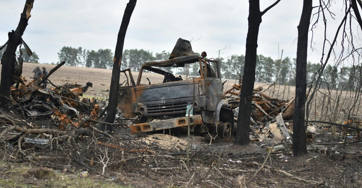 Charred remains of a truck in a war-torn forest area with burnt trees