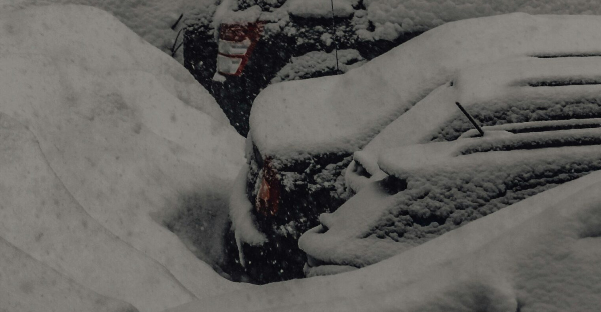 Heavy snow blankets parked cars in a quiet urban setting on a winter day.