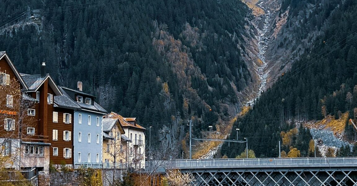 Picturesque view of Göschenen village with a bridge, river, and snow-capped mountains in autumn.
