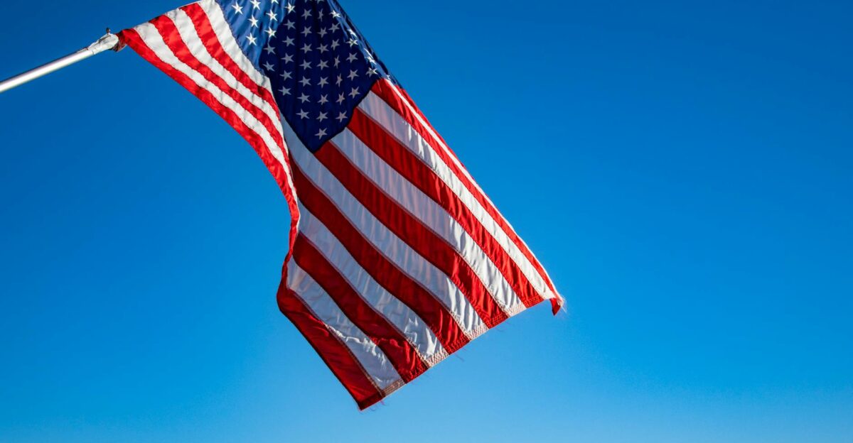 The American flag proudly waves on a flagpole against a clear blue sky symbolizing freedom and patriotism