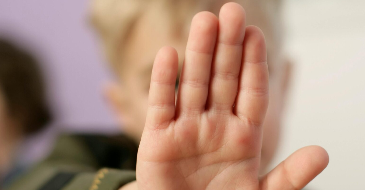 A child making a stop gesture with an open hand indoors.