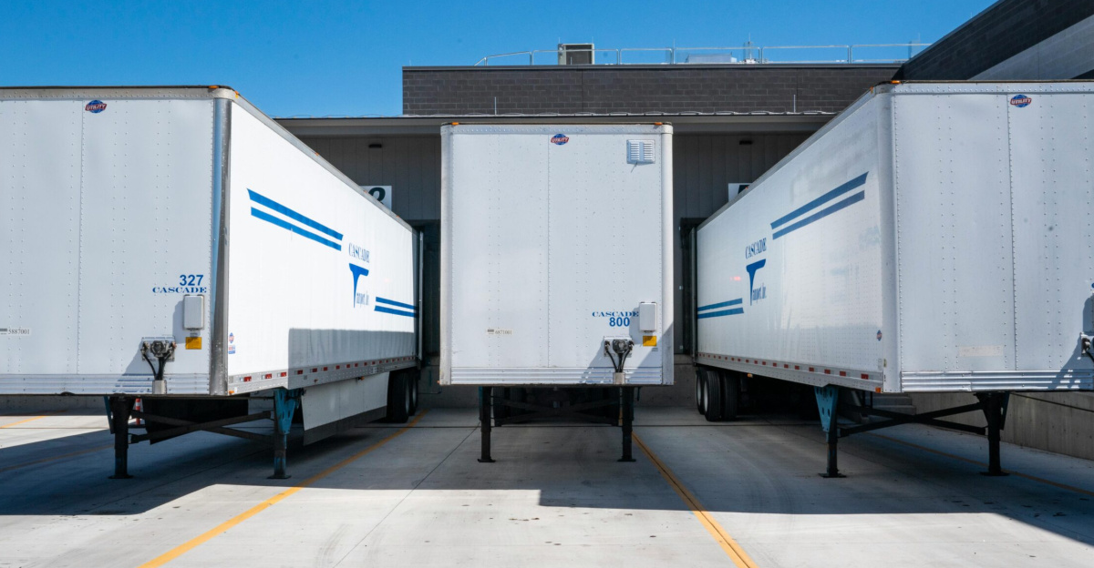 Three white cargo trailers parked at an industrial shipping dock under clear blue skies.