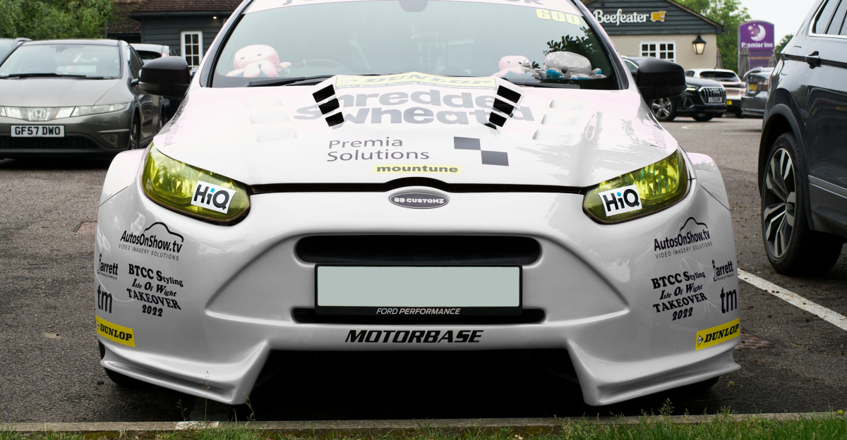 Front view of a modified Ford car in a parking lot in Whitstable, UK, showcasing various decals and sponsorships.