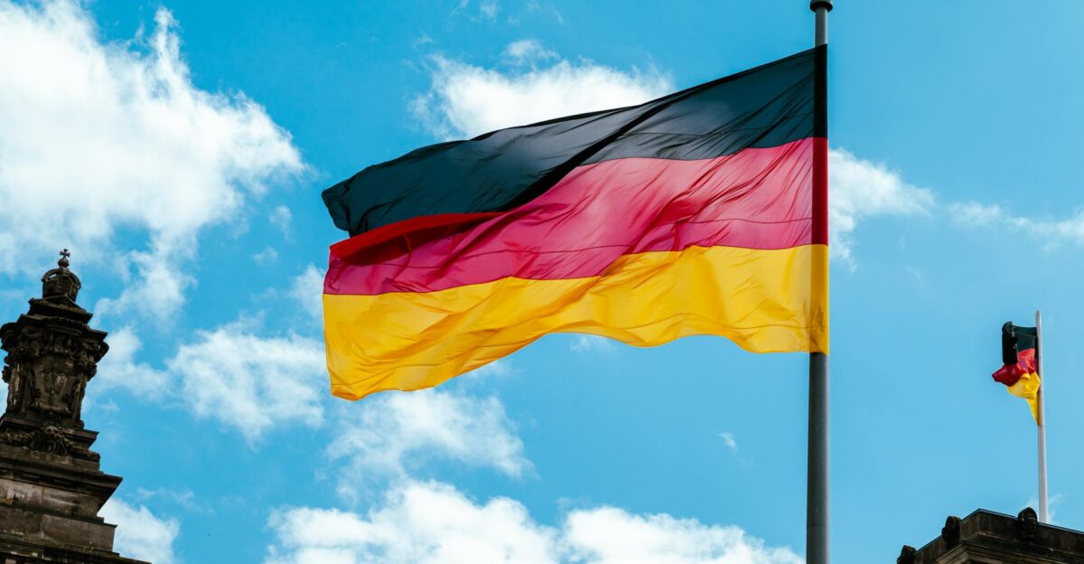 Vibrant German flag waving on a flagpole against a bright blue sky with clouds
