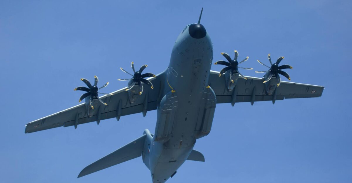 Low angle view of a large military airplane in flight against a clear blue sky