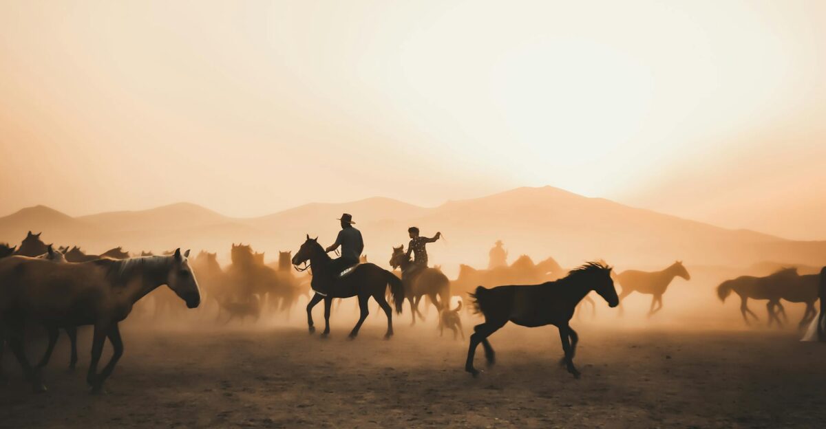 Silhouetted cowboys on horses herding a dusty herd at sunset with dramatic lighting and dusty ambiance