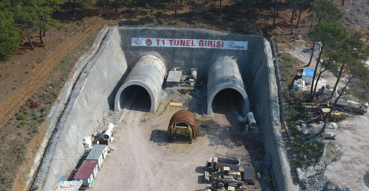 Aerial shot of Yeniçam tunnel construction site in Çanakkale, Turkey, showcasing heavy machinery and forest surroundings.