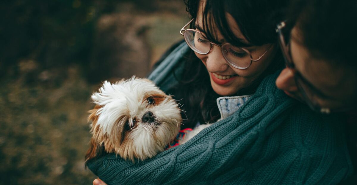 A woman lovingly cuddles her Shih Tzu puppy wrapped in a warm blanket outdoors