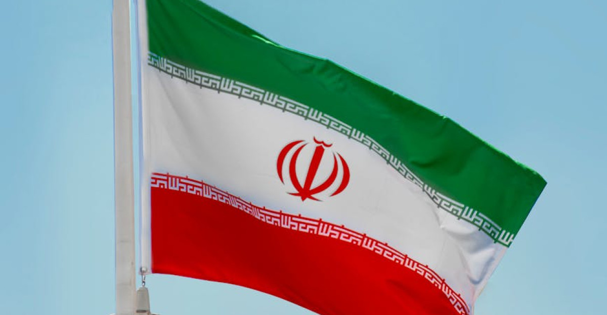 Low-angle view of the Iranian flag waving on a flagpole against a clear blue sky in Tehran Iran