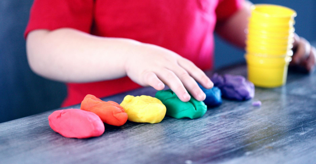A young child with rainbow-colored modeling clay and stacking cups on a table indoors