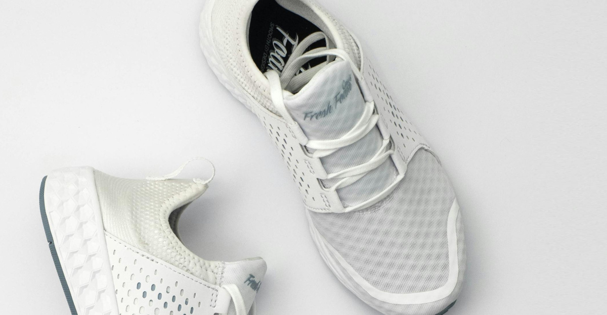 Pair of modern white sneakers with laces on a neutral backdrop.