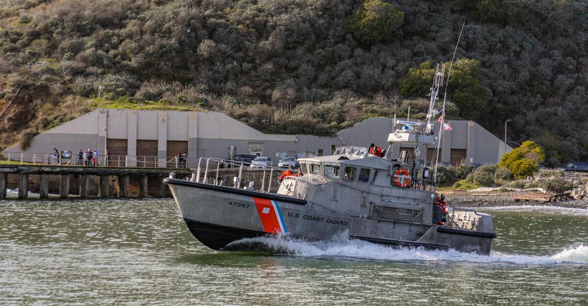 Operational U S Coast Guard boat cruising near seashore facility in daylight