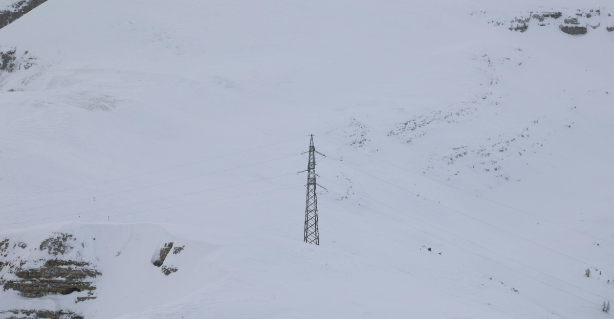 Expansive snowy mountain landscape featuring a lone power line tower.