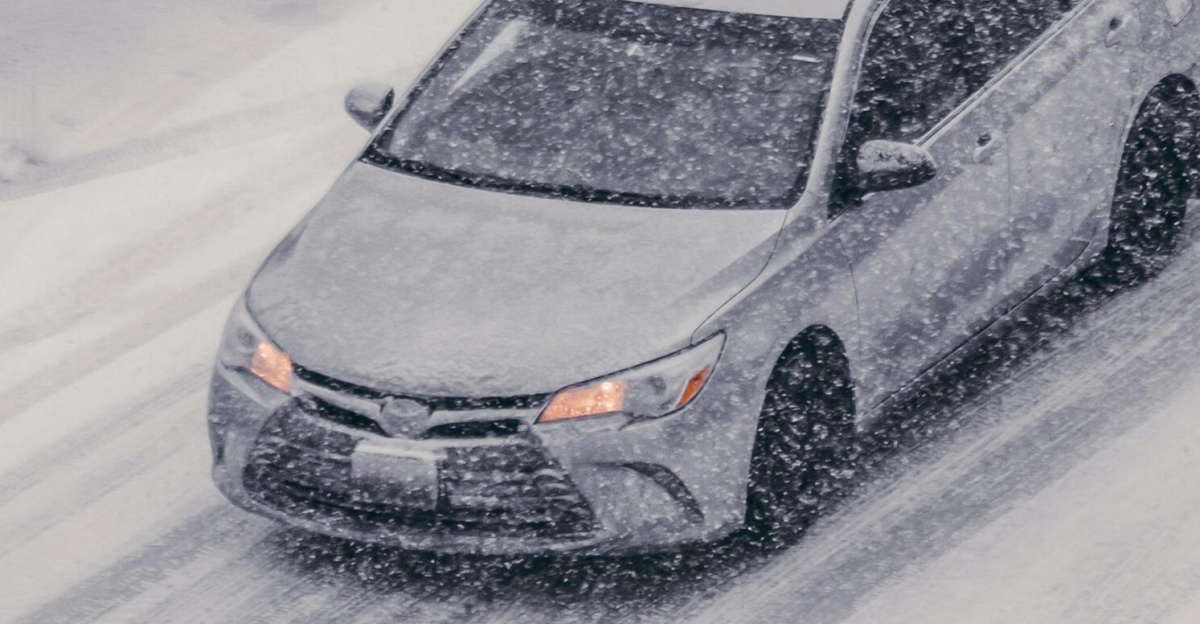 Car driving through heavy snowstorm on icy street, showcasing winter weather challenges.