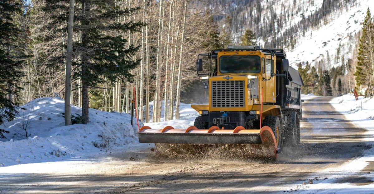 A snowplow clearing a snow-covered mountain road surrounded by trees in Winter Park CO