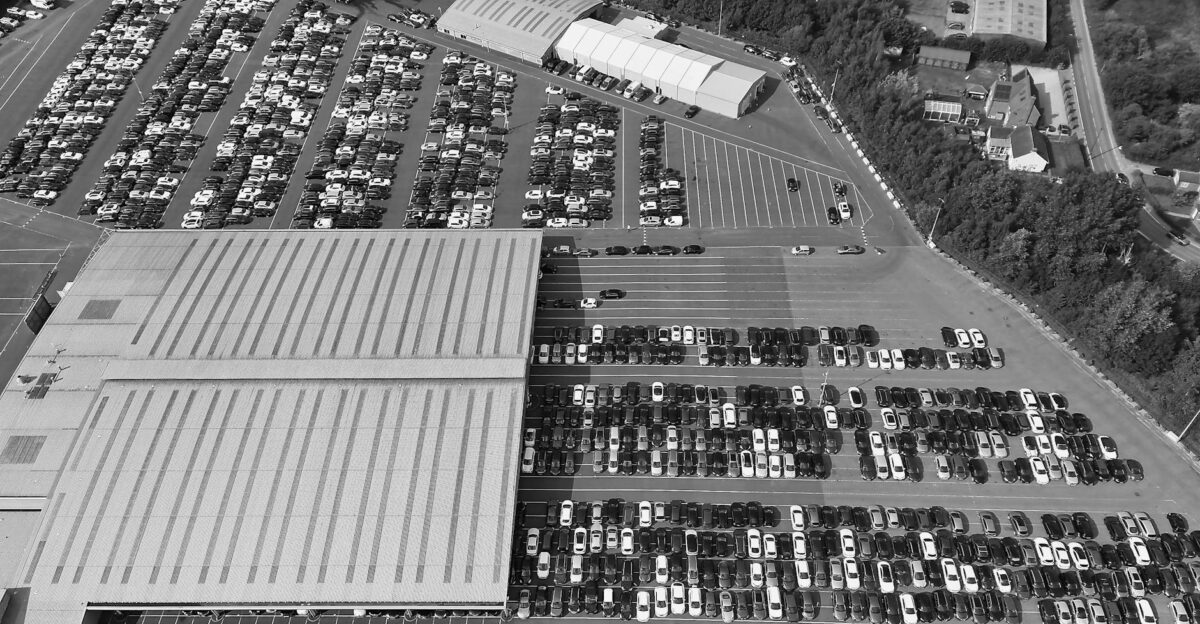 An expansive black and white aerial view of a crowded parking lot with rows of parked cars
