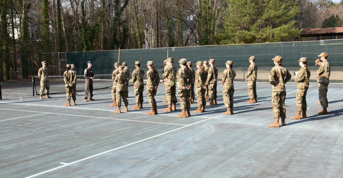 Soldiers in uniform standing in formation on an outdoor tennis court during the day