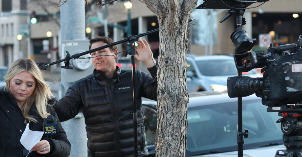 News crew setting up equipment on city street, capturing urban life.