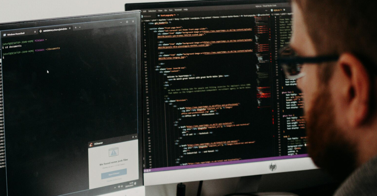 Software developer typing code on dual monitors at a wooden desk.