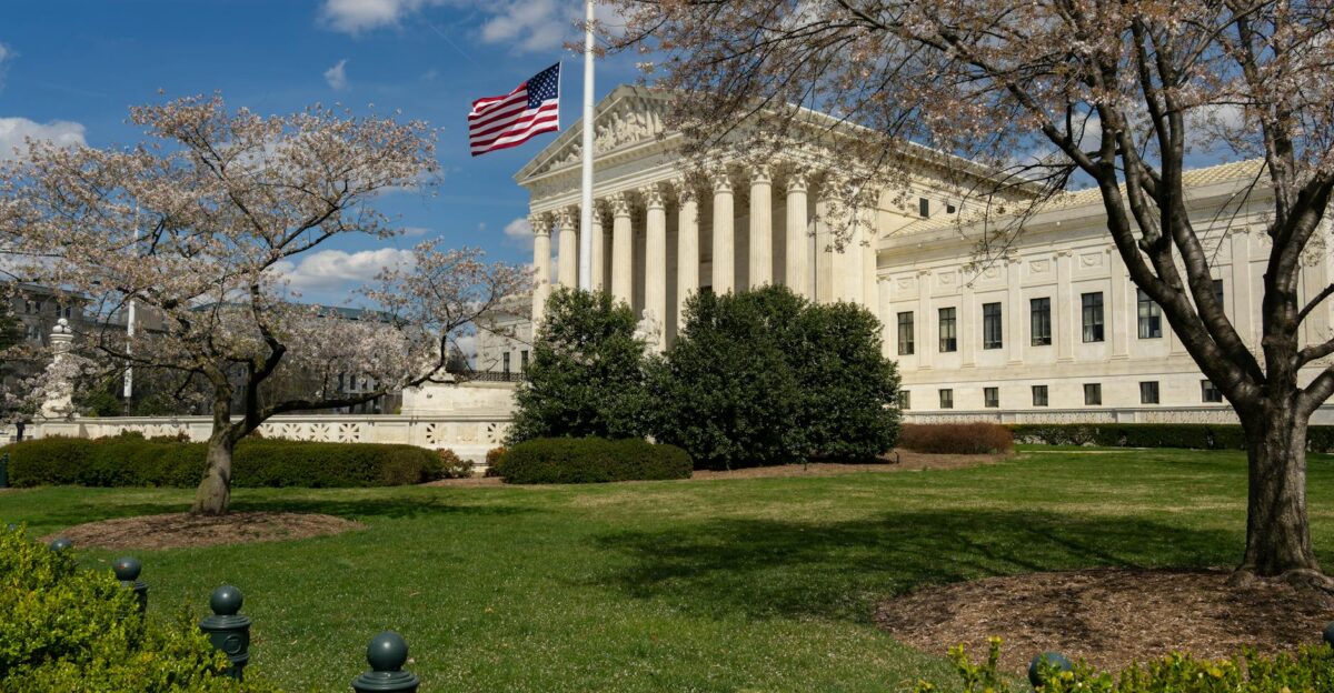 A view of a neoclassical government building with an American flag and cherry blossoms in Washington DC