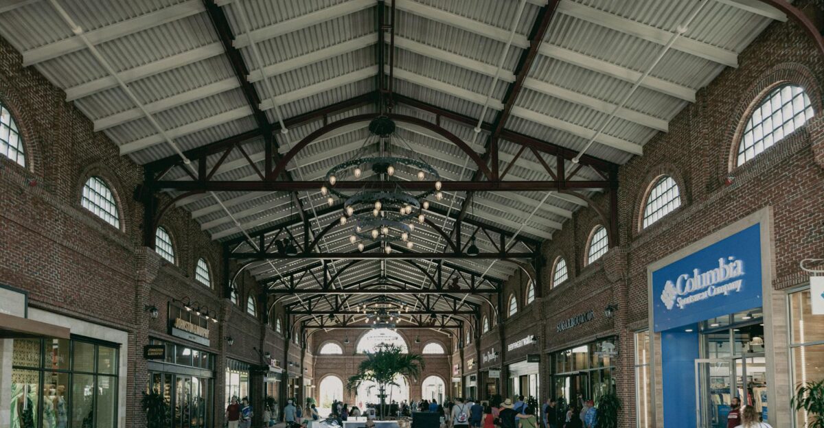 Urban shopping mall interior with people walking amid stores under decorative lighting and exposed beams