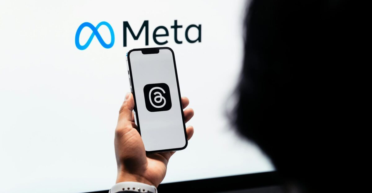 Hands holding smartphone with Meta Threads logo on screen Meta branding in background
