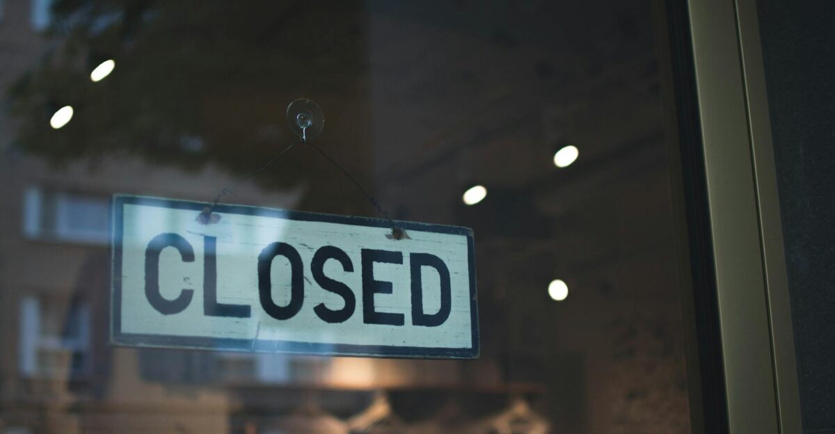 A closed sign hangs on a glass window of a modern urban storefront