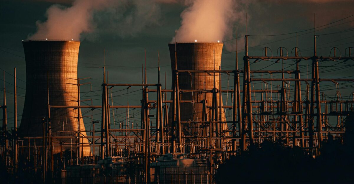 A nuclear power plant s cooling towers emit steam at sunset highlighting industrial infrastructure