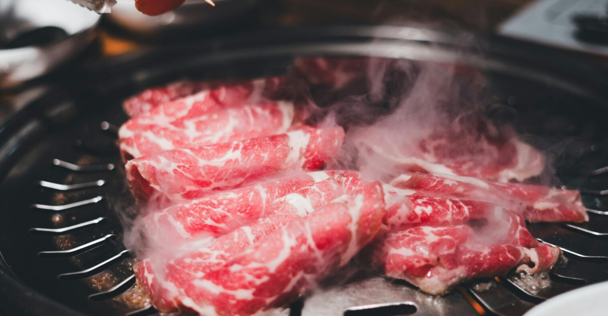 Appetizing grilled meat steaming on an indoor BBQ at a restaurant, with various sides on the table.