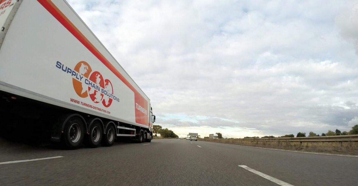 A large semi truck labeled Supply Chain Solutions travels down a highway under a cloudy sky