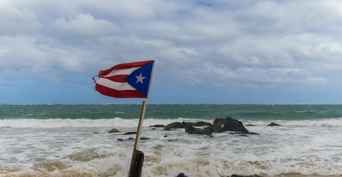 A Puerto Rican flag waves on a rocky beach under a cloudy sky capturing a sense of national pride