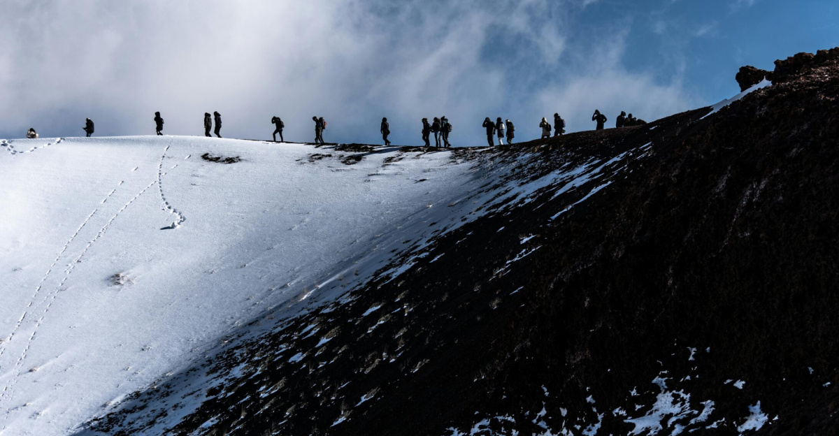 Adventurers trekking the snowy slopes of Mount Etna in Sicily, Italy under a dramatic sky.
