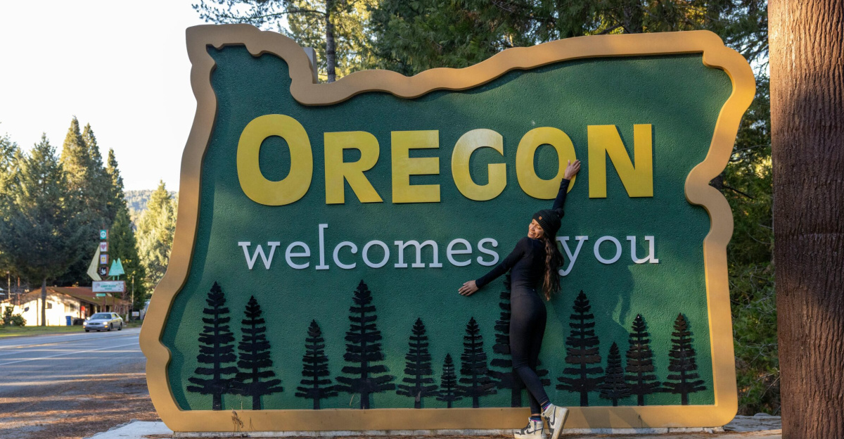 A woman joyfully poses with the iconic Oregon welcome sign on a sunny day.