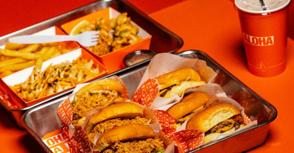 A vibrant display of burgers fries and a drink on an orange background