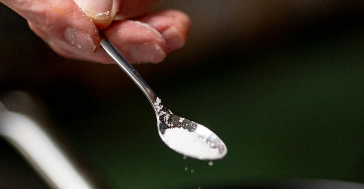 Close-up of a hand sprinkling salt onto sliced onions cooking in a frying pan.