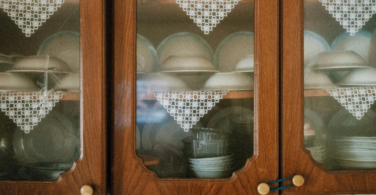 Vintage porcelain cups and plates elegantly displayed in wooden cabinets with lace decor.
