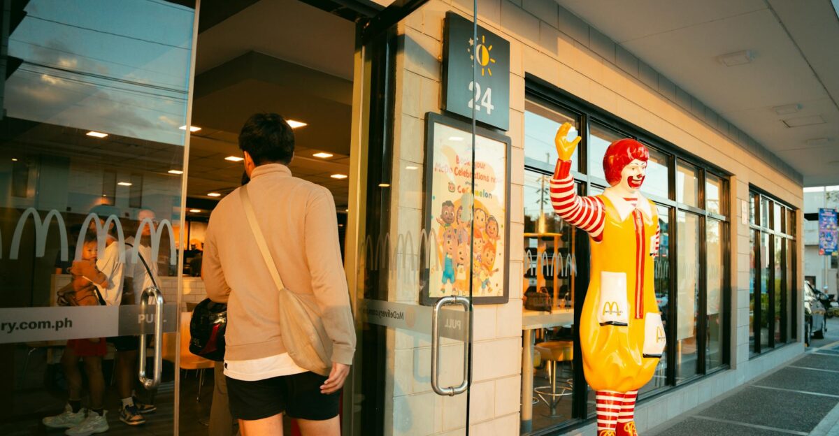 A man in casual attire enters a McDonald s restaurant past a Ronald McDonald statue during daylight