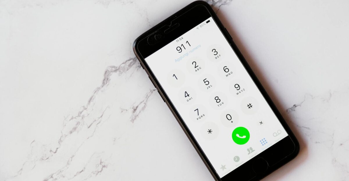 Close-up of a smartphone displaying the emergency number 911 on a white marble surface