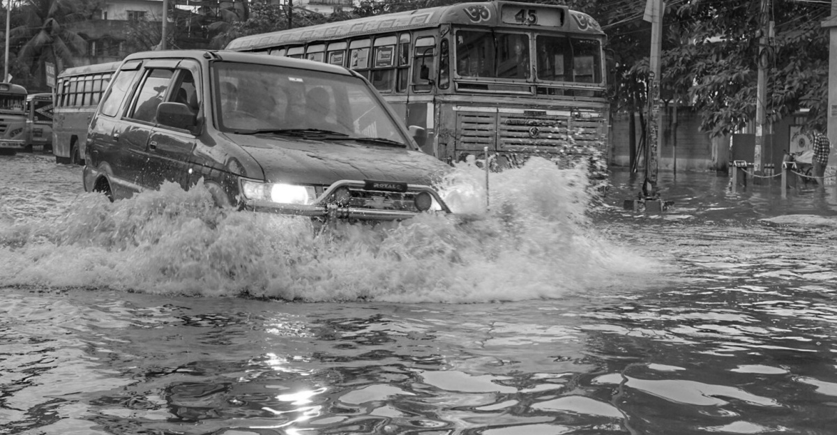 Flooded street scene in Kolkata, India, showcasing vehicles and people affected by monsoon rains.