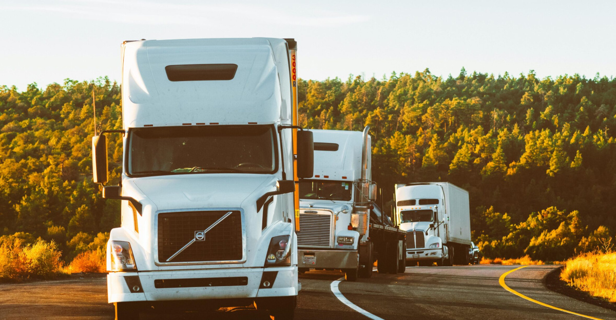 Three semi trucks driving on a highway through a forested landscape in Arizona.