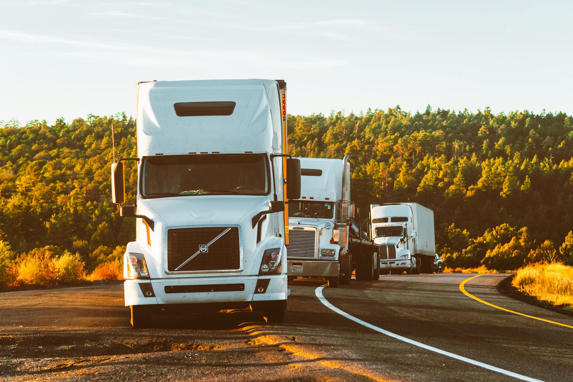 Three semi trucks driving on a highway through a forested landscape in Arizona