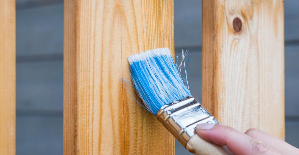 A hand painting a wooden fence plank with a blue paintbrush outdoors Perfect for DIY and renovation themes