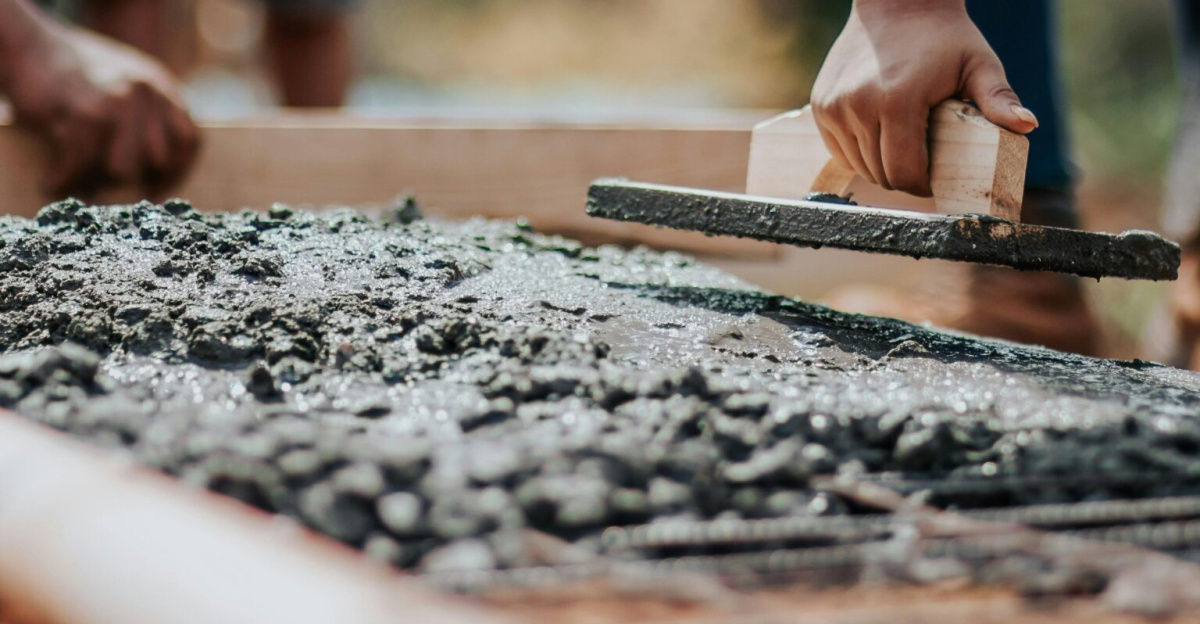 Construction workers leveling fresh cement on a sunny day at an outdoor site.