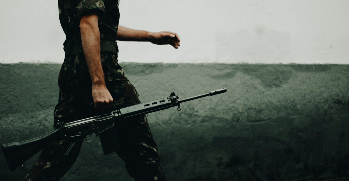A soldier in camouflage walking with a rifle against a textured wall day