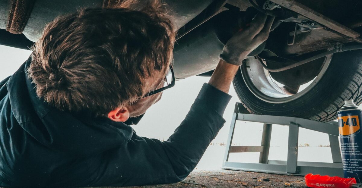 Mechanic skillfully repairing car undercarriage in outdoor setting with tools