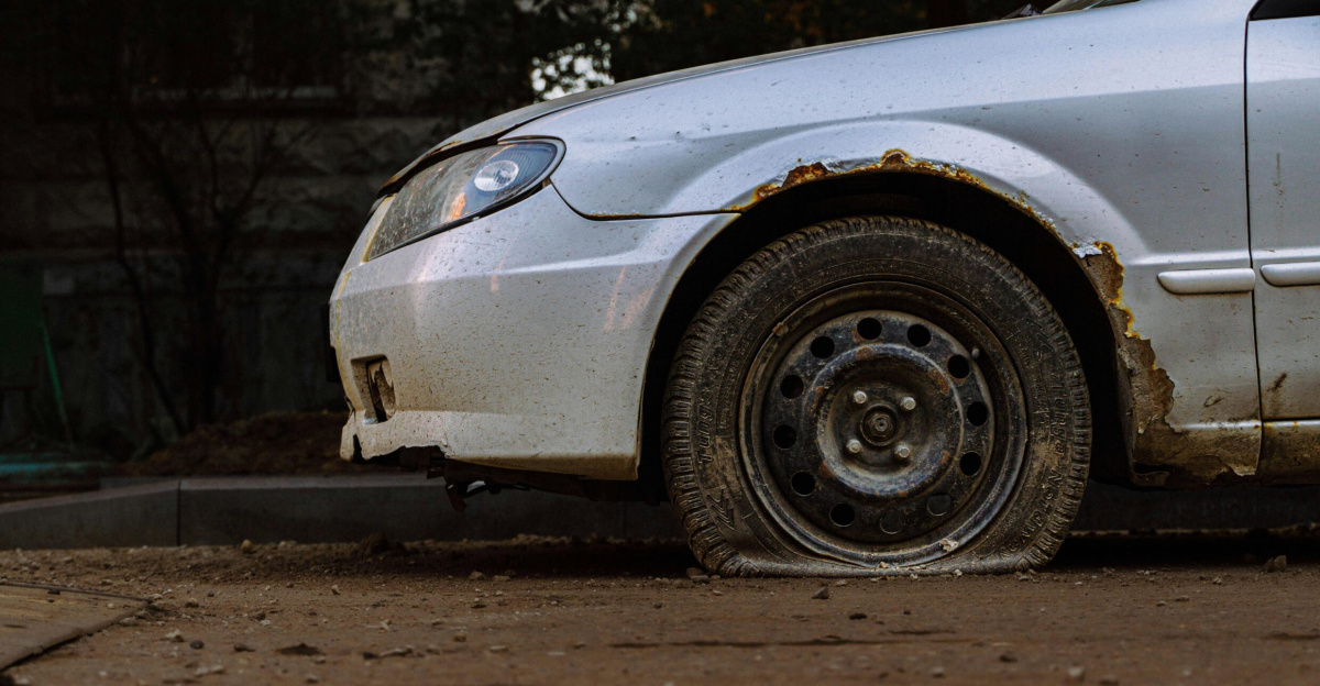 Close-up of a rusted car with a flat tire parked on a street in Moscow, illustrating urban decay.