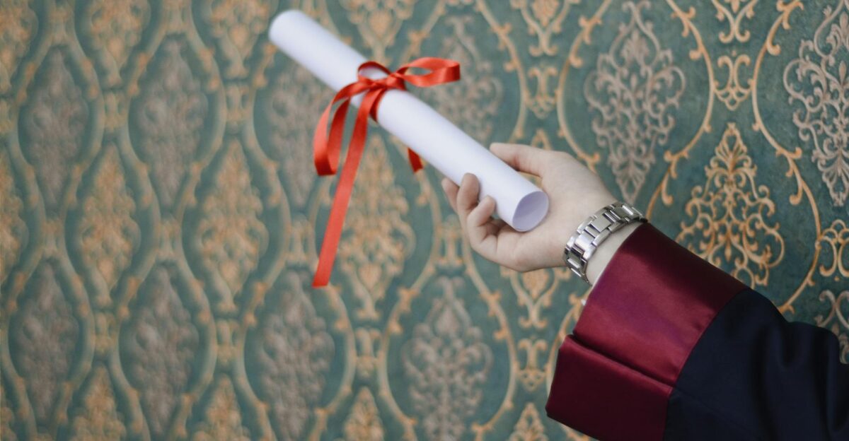 A graduate s hand holding a diploma with red ribbon symbolizing achievement