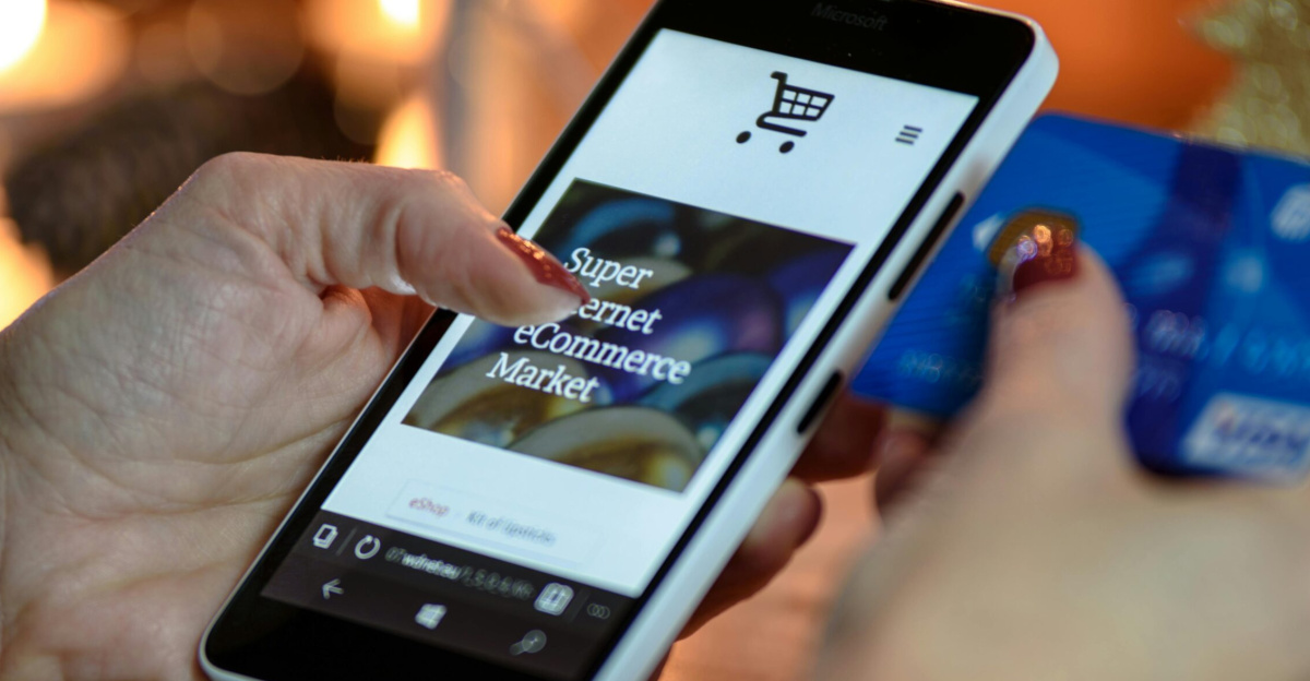 Woman using smartphone for online shopping with credit card in hand, festive background lighting.